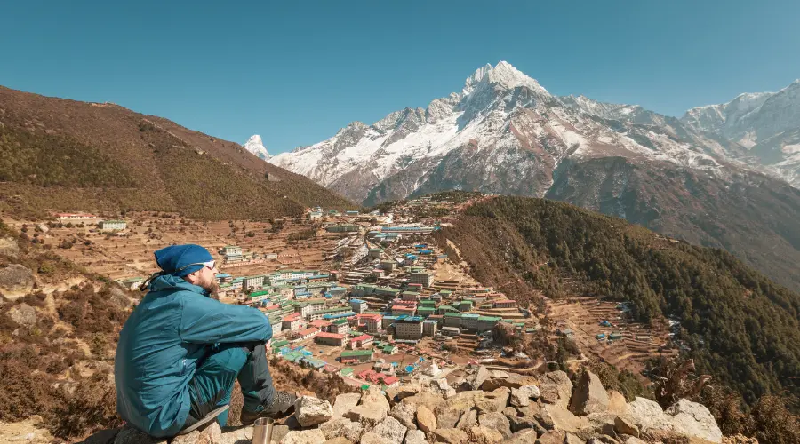 A trekker sitting on floor enjoying view of the Namche Bazaar route to EBC