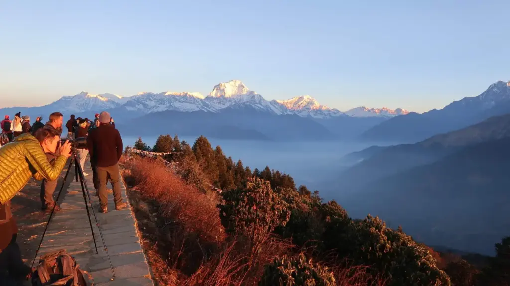 Trekkers and photographers capturing a golden sunrise over the snow-capped Annapurna range from Ghorepani Poon Hill, a popular choice for monsoon treks in Nepal.