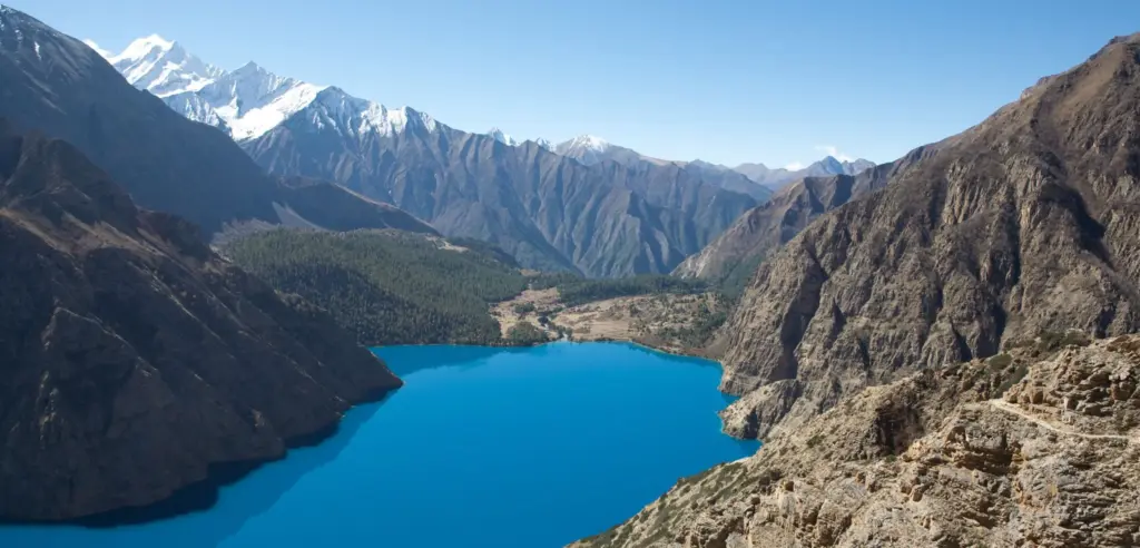 Panoramic view of the vibrant blue Phoksundo Lake in Lower Dolpo surrounded by rugged, arid mountains, highlighting scenic monsoon treks in Nepal.